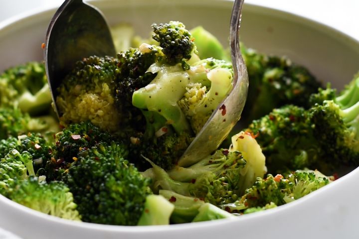 Pan fried broccoli florets being lifted by two spoons with garlic and red pepper flakes.
