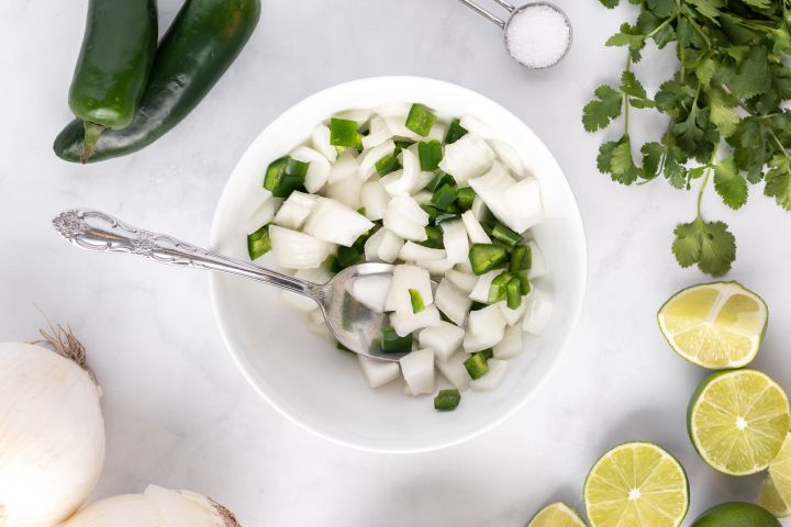 Diced onions and jalapenos in a bowl with lime juice.
