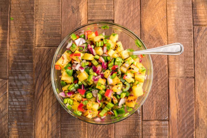 Pineapple salsa with cilantro, red peppers, red onion, serrano peppers, and lime juice in a bowl.