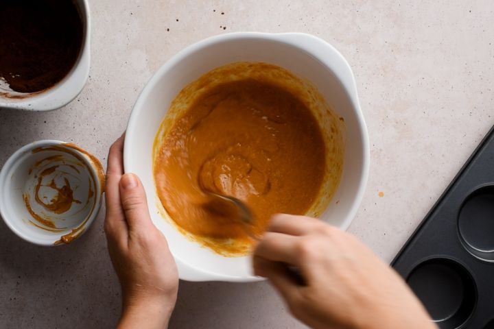 Pumpkin, eggs, almond butter, and maple syrup being stirred in a bowl.