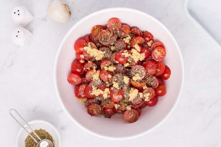 Grape tomatoes in a bowl tossed with minced garlic, black pepper, salt, Italian seasoning, and olive oil.
