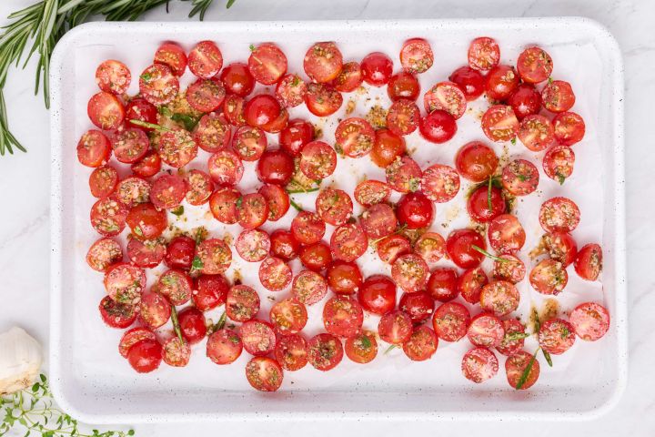 Grape tomatoes tossed in herbs and olive oil on a baking sheet.