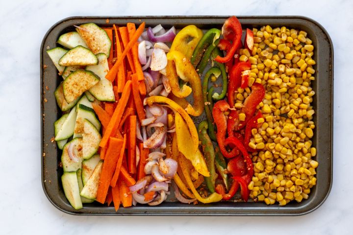 Zucchini, carrots, bell peppers, red onion, and corn on a baking sheet.