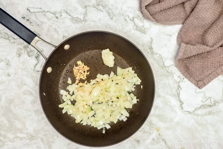 Onions, ginger, garlic, and jalapenos cooking in a skillet.
