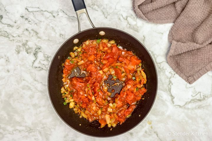 Diced tomatoes being added to an onion and spice mixture.