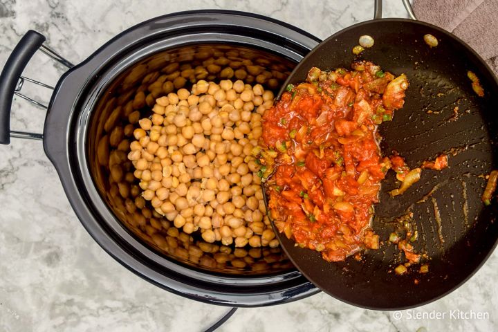 Tomato mixture being poured over chickpeas in a slow cooker for chana masala.