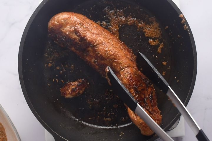 Pork tenderloin being seared in a hot cast iron skillet.