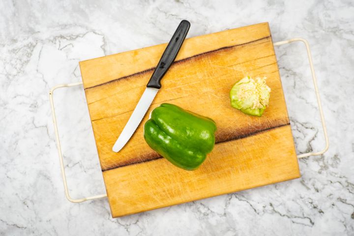 Green bell pepper on a cutting board with the top and seeds removed.
