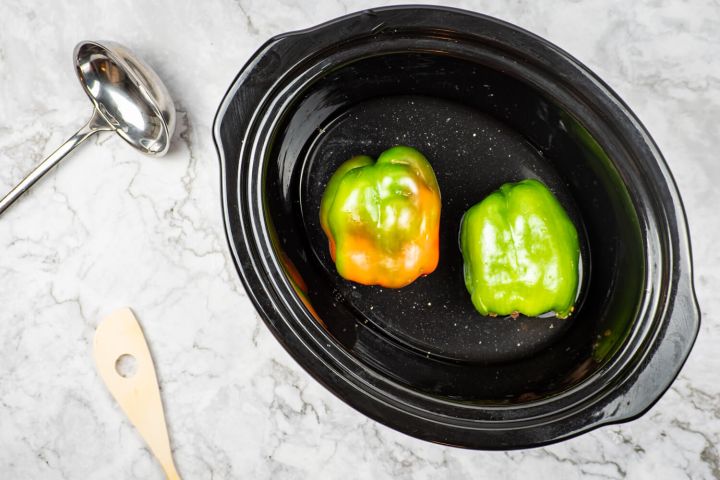 Green bell peppers in the slow cooker with water for cooking.