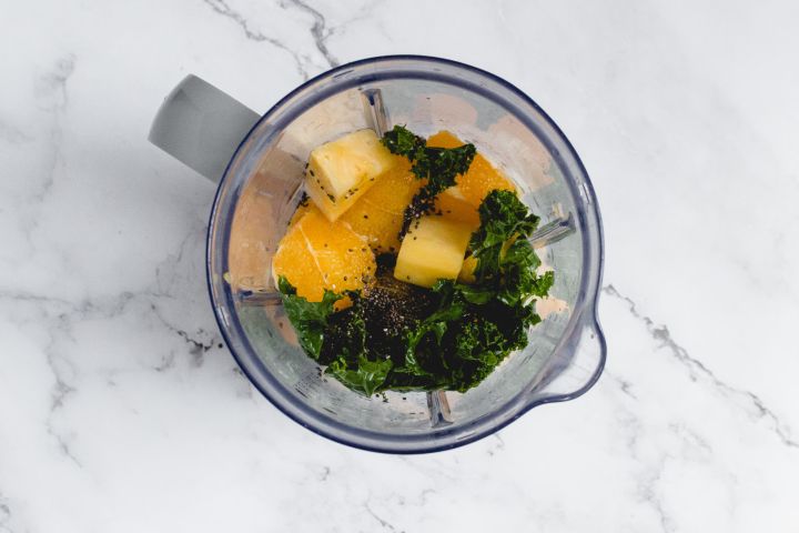 Mango, pineapple, and chia seeds added to a kale smoothie in a blender.