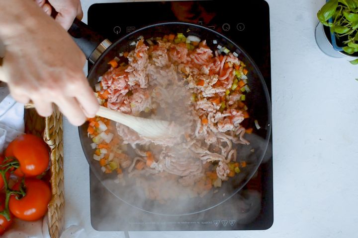 Ground turkey, carrots, celery, and onion being cooked in a skillet.