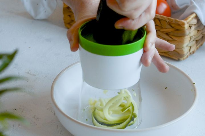Zucchini noodles being made with a spiralizer over a white plate.
