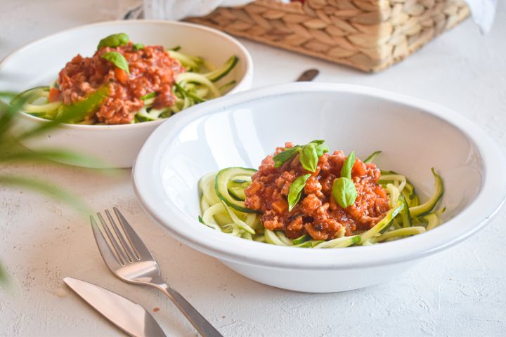 Zucchini noodle bolognese in two white bowls with fresh basil and sauce.