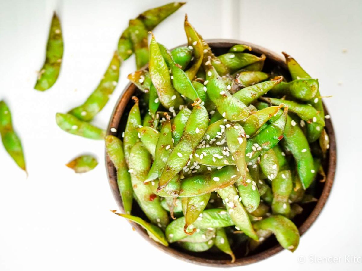 Stir fried edamame in a wooden bowl served with soy sauce and sesame seeds.