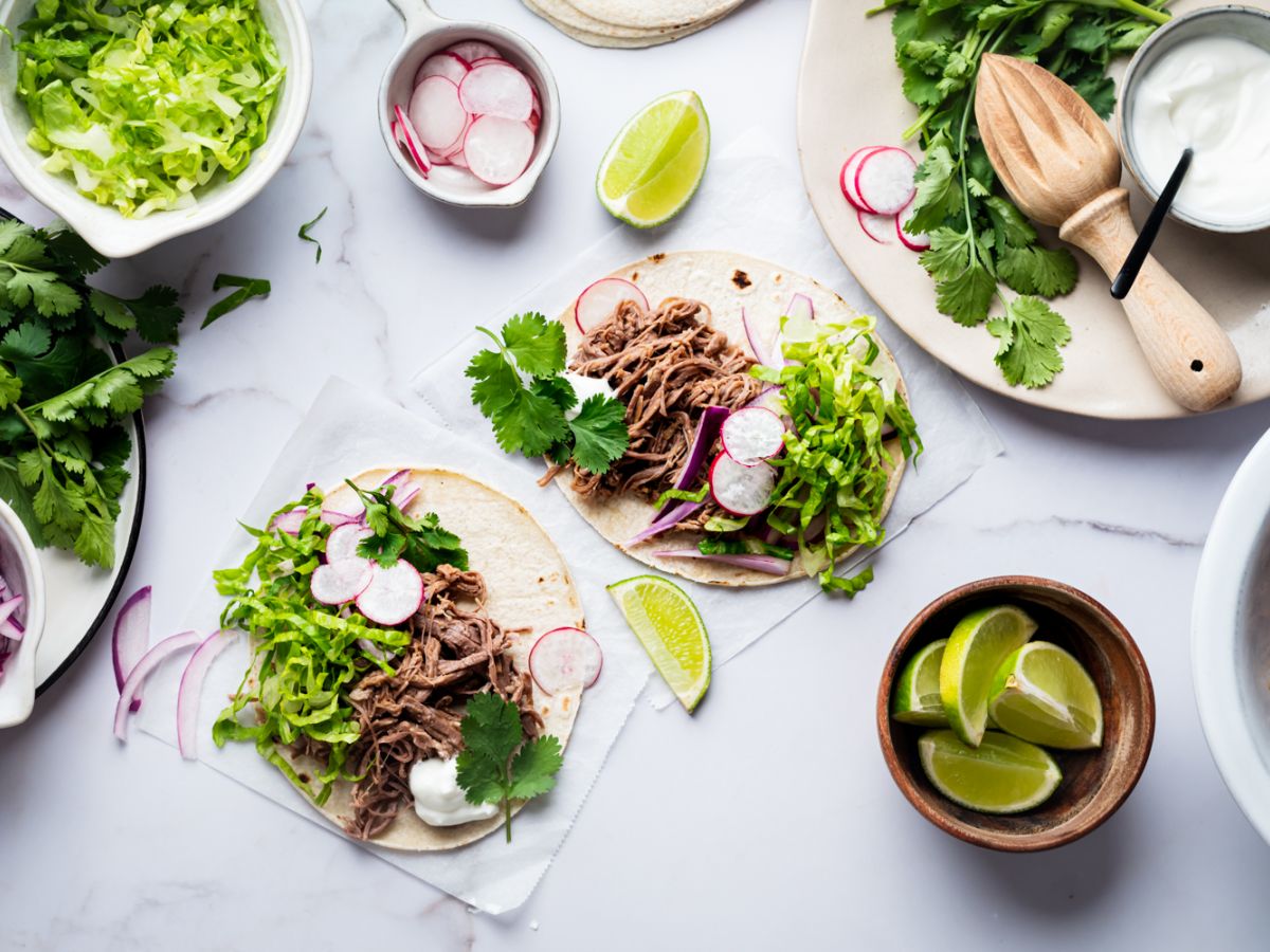 Crockpot tri-tip shredded tacos with red onion, cilantro, lettuce, and radishes served on corn tortillas.