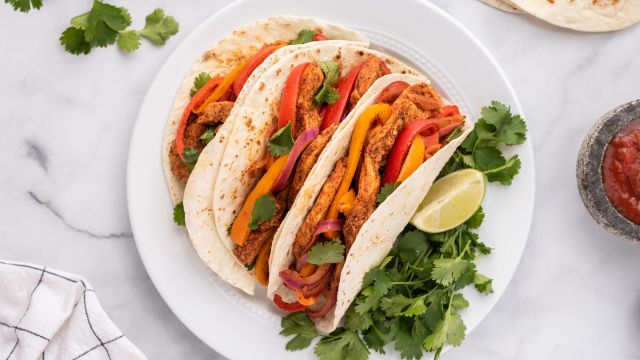 Chicken fajitas topped with peppers, onions, cilantro, and lime in flour tortillas.