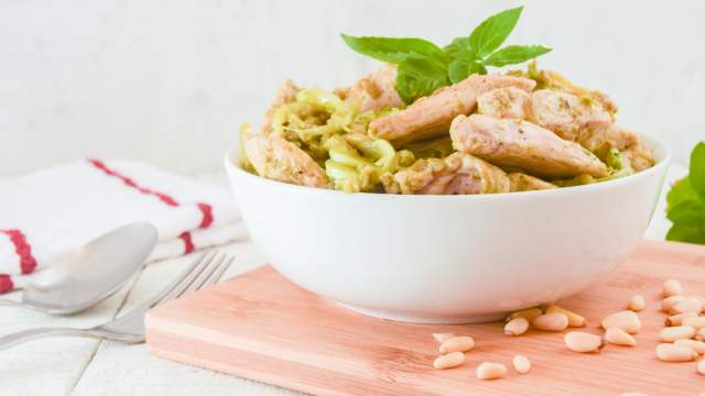 Pesto zoodles with chicken in a bowl with pine nuts on the side.