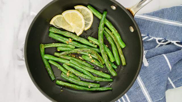 Garlic green beans in a skillet with fresh lemon slices.