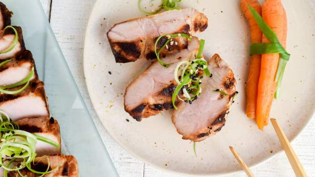 Asian grilled pork tenderloin on a plate with carrots, green onions, and chopsticks.