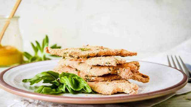 Parmesan crusted chicken piled on a plate with fresh basil and a fork.