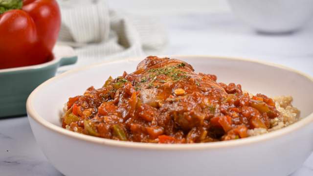 Slow cooker chicken cacciatore in a bowl with tomato sauce, chicken, mushrooms, and peppers over quinoa.