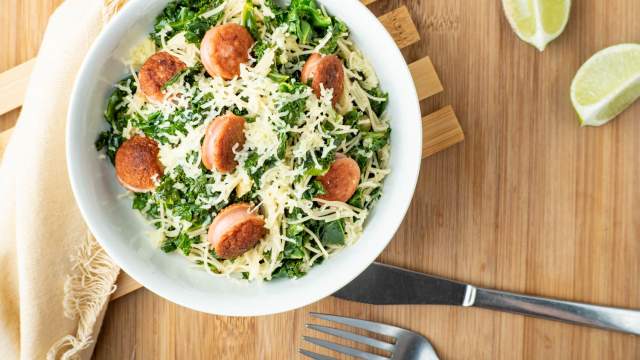 Angel hair pasta with sausage and kale in a bowl with a fork and knife.