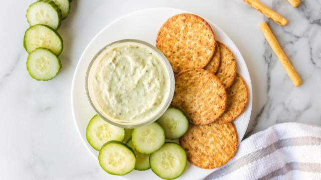 Avocado ranch dip with Greek yogurt served in a small bowl with sliced cucumbers and crackers.