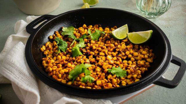Blackened corn with homemade seasoning served in a skillet with lime wedges and cilantro.