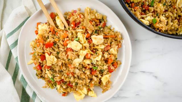 Cauliflower fried rice with cabbage, carrots, eggs, and green onions on a plate with chopsticks.