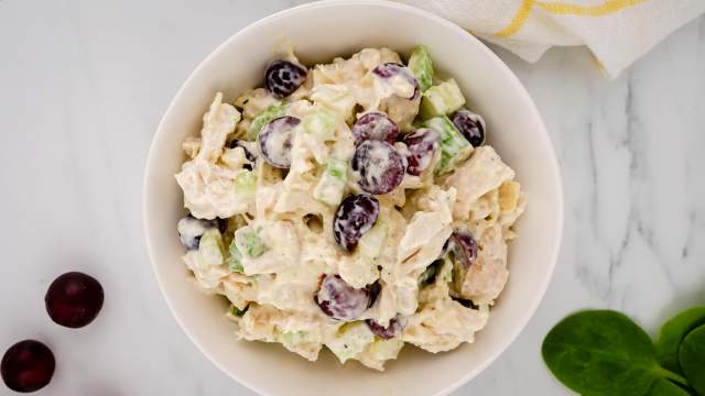 Chicken salad with grapes, celery, and yogurt dressing in a bowl with grapes and spinach on the side.