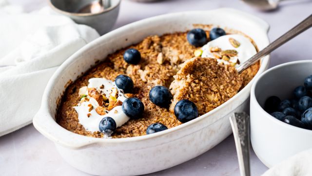 Cinnamon baked oatmeal with rolled oats baked in a white dish topped with blueberries and honey.