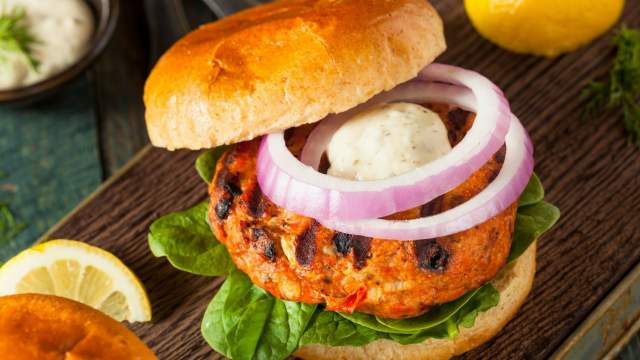 Curry salmon burgers with yogurt sauce on a bun with red onion and herbs.