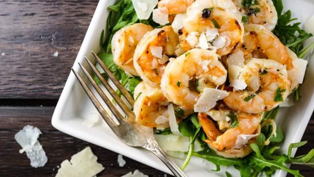Garlic Parmesan shrimp on a plate with pieces of Parmesan cheese and greens.