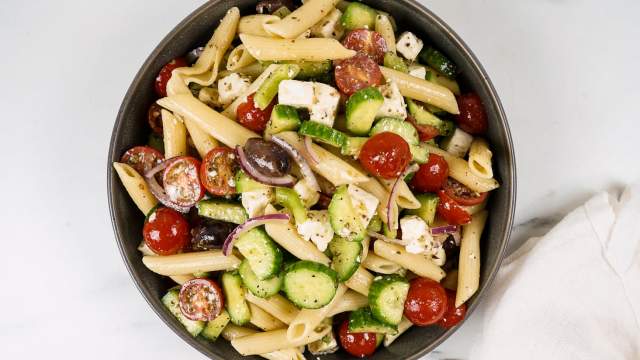 Greek pasta salad with tomatoes, cucumbers, black olives, feta cheese, and Greek dressing in a bowl. 