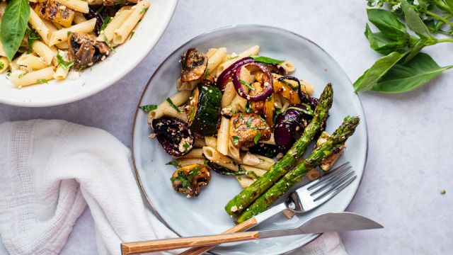 Grilled vegetable pasta salad with balsamic dressing, mushrooms, zucchini, asparagus, red onion, and herbs on a plate.