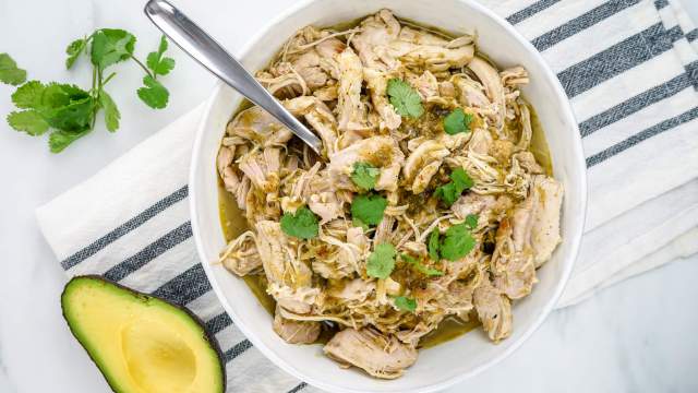 Instant Pot Salsa chicken shredded in a bowl with green salsa and cilantro.