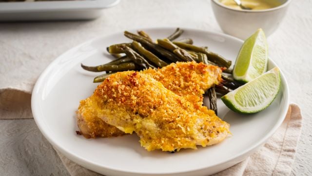 Sheet pan lemon pepper chicken coated with breadcrumbs and Parmesan cheese on a plate with roasted green beans,