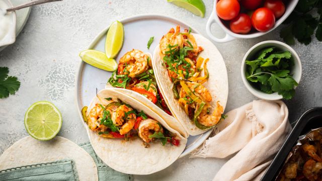 Sheet pan shrimp fajitas with peppers and onions served on flour tortillas with lime and cilantro.