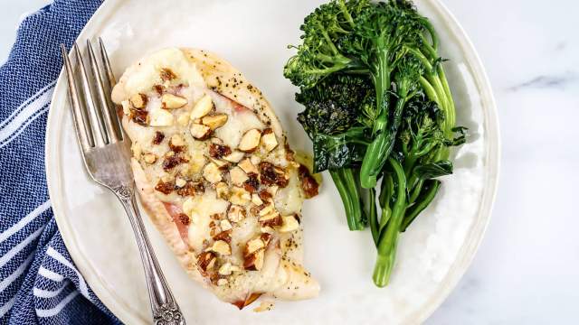 Chicken cordon bleu with ham and melted Swiss cheese on a plate with broccoli.