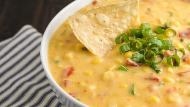 Corn dip with cheddar cheese, tomatoes, jalapeno, onion, and corn in a bowl.