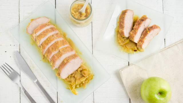 Slow Cooker Pork Tenderloin on a bed of apples and onions with a green apple on the side.