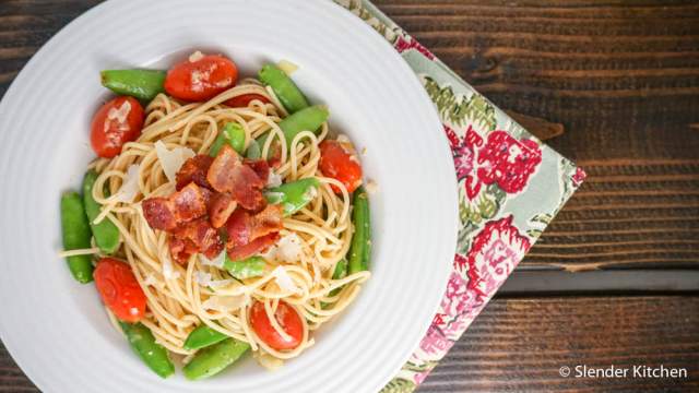 Snap pea pasta with bacon, cherry tomatoes, Parmesan cheese, and lemon in a white bowl.