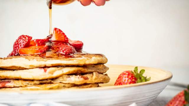 Strawberry Banana Oat Pancakes with maple syrup being poured on top.